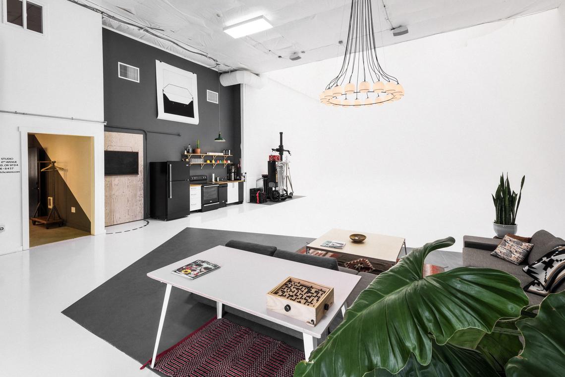 Wide view of the studio lounge — white table, rug, and kitchen along the wall